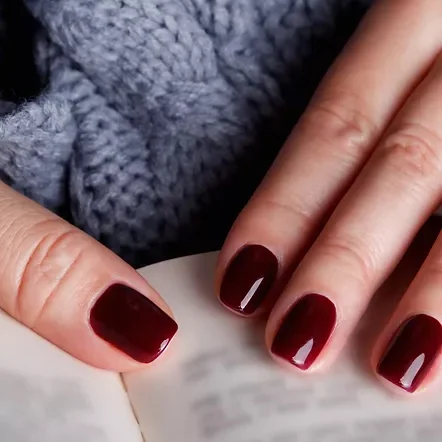 Glossy oxblood acrylic nails against a grey knit sleeve